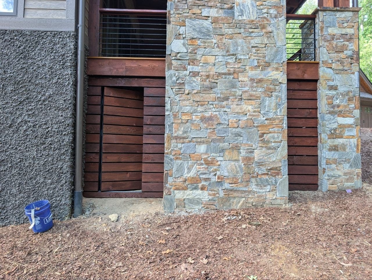Wood access panel swung open on its hinge, set into a stone porch column, stained dark to match the horizontal skirting boards around it.