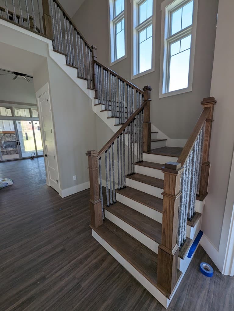 Finished interior staircase with stained wood treads, newel posts and iron balusters, open to a great room